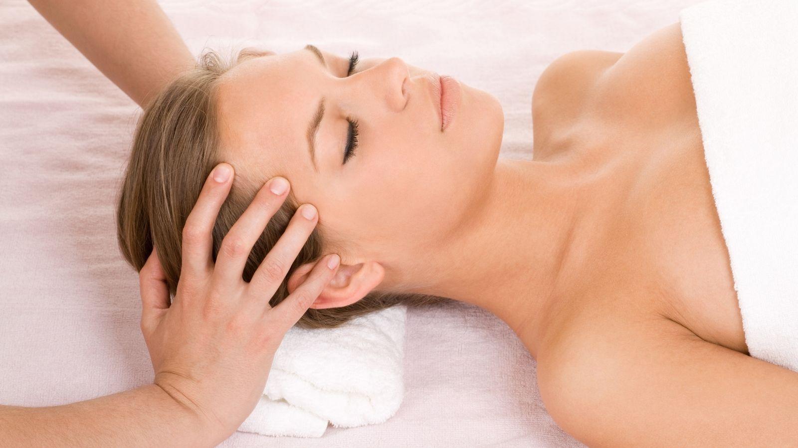 Image of a lady lying down having Indian Head Massage Boroughbridge. The lady has brown hair and has hands on her head. She is wearing a white towel