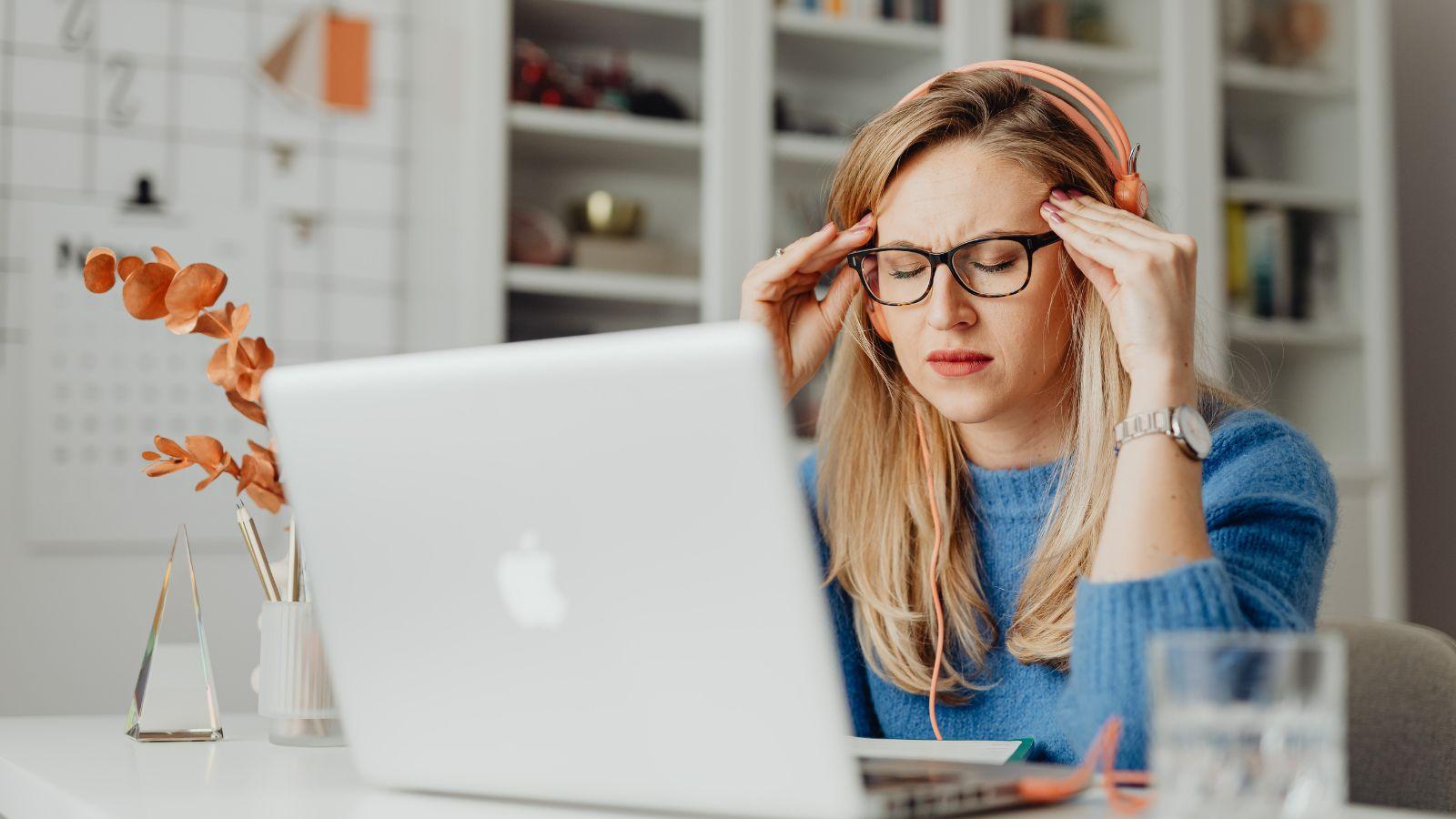 What causes headaches .Image of woman holding head next to laptop