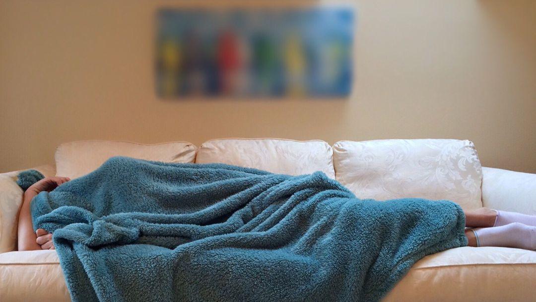Seasonal Affective disorder : image of exhausted person asleep on sofa under a blue blanket