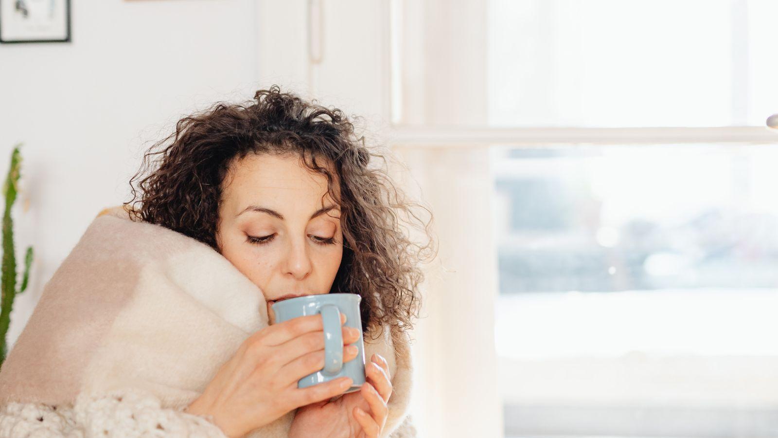 overcome stress - image of woman wrapped in a blanket drinking a hot drink from a blue mug