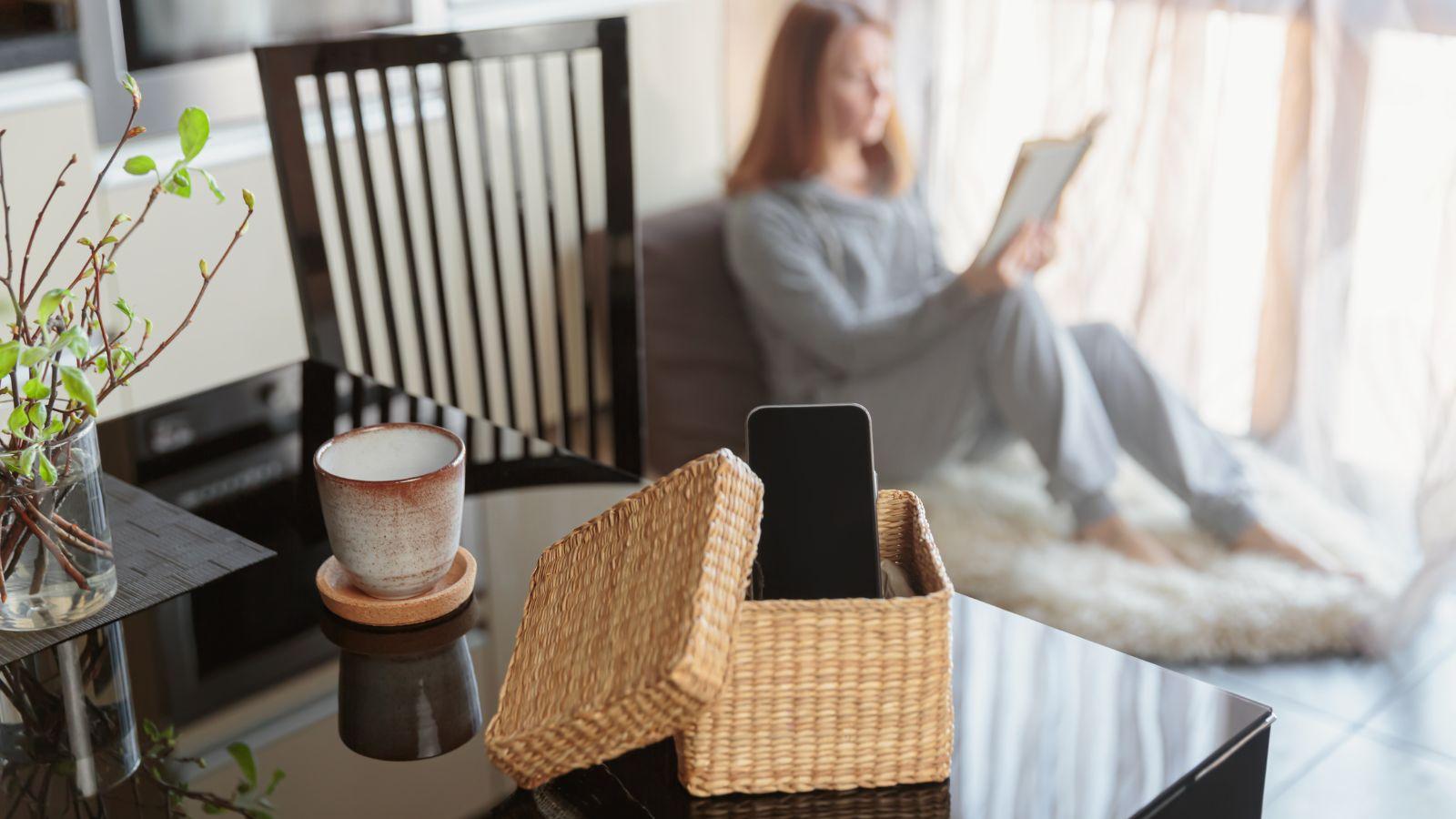 autumn self care tips digital detox, image of woman sitting in chair reading whilst her mobile phone is in a basket out of the way
