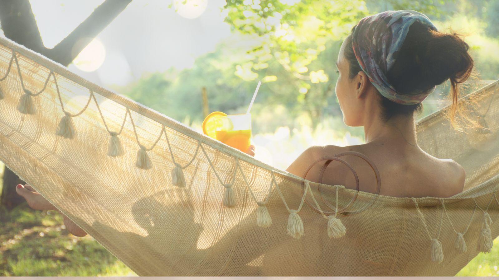 Summer energy rest image of woman lounging in hammock in garden, she has dark hair which is tied back