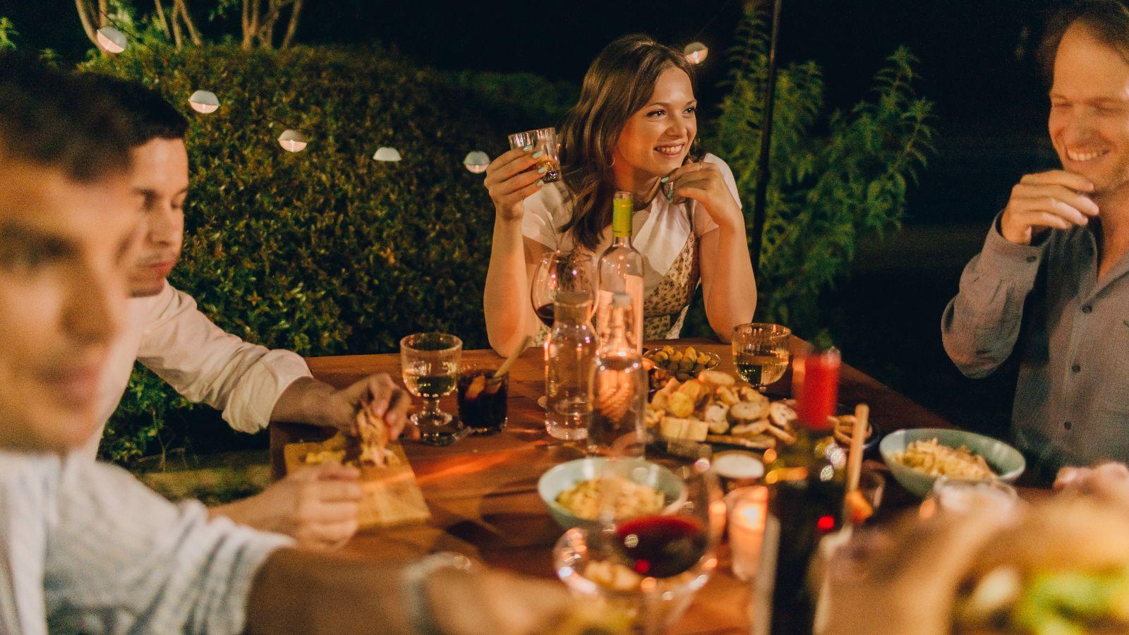 Summer energy image of friends sat around a table dining al fresco with tapas and a bottle of red wine