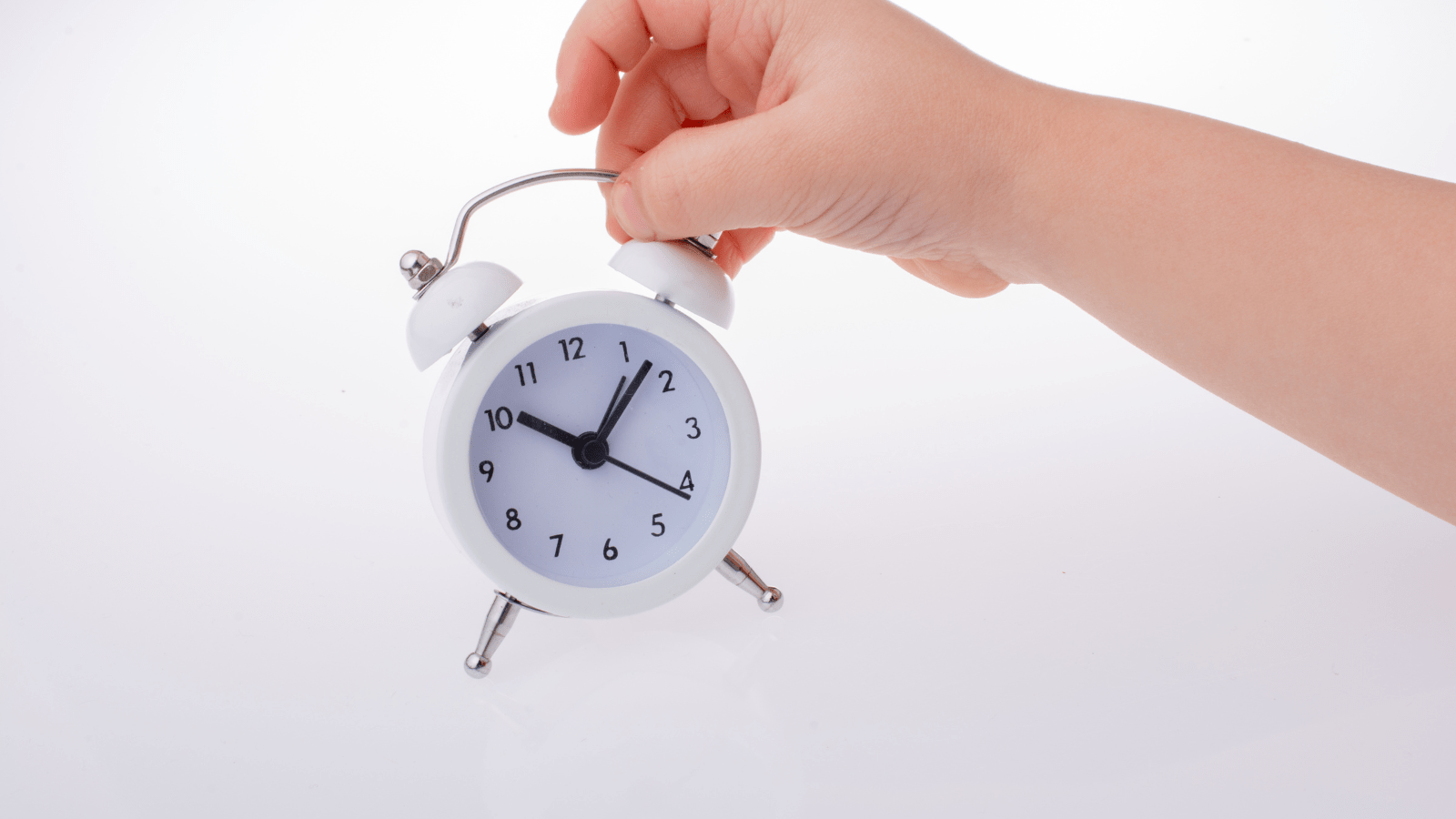 Calm the chaos power hour image of a hand holding a white traditional style alarm clock to illustrate the point of power hour to calm the chaos