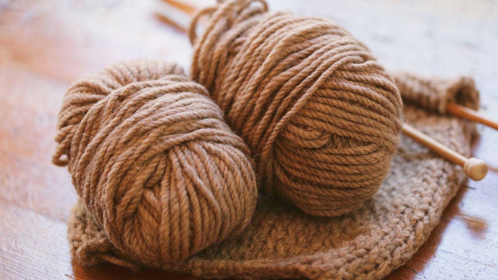 image of some autumn coloured wool on knitting needles on a pink background