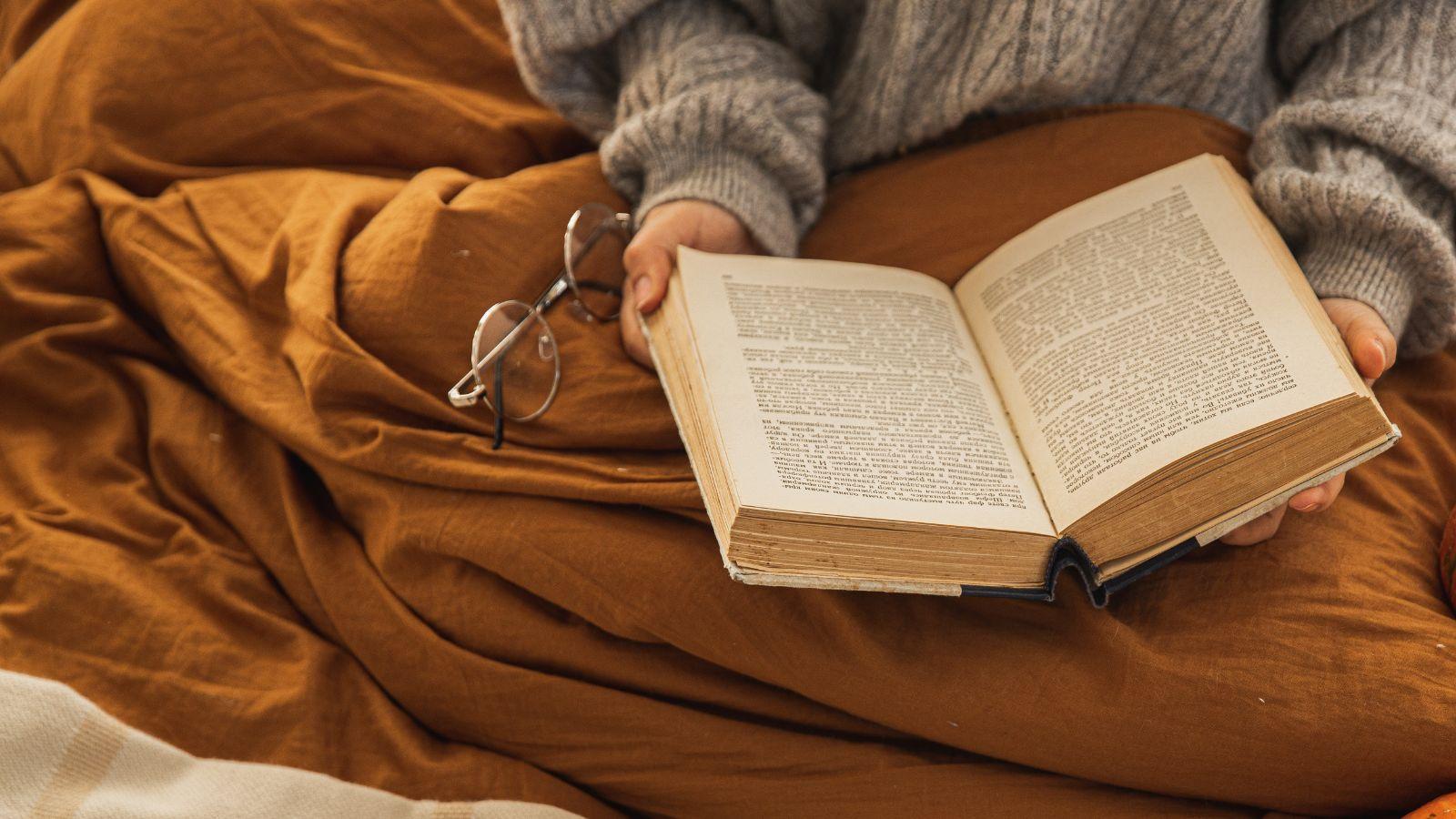image of a rusty coloured blanket and lady reading a book to depict autumn