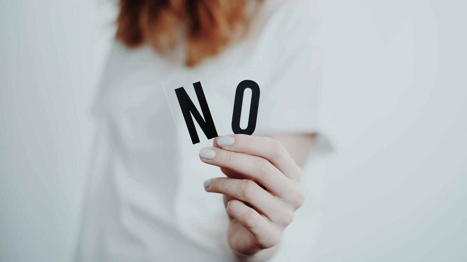 Image of woman holding the word no to illustrate how to be more goddess like