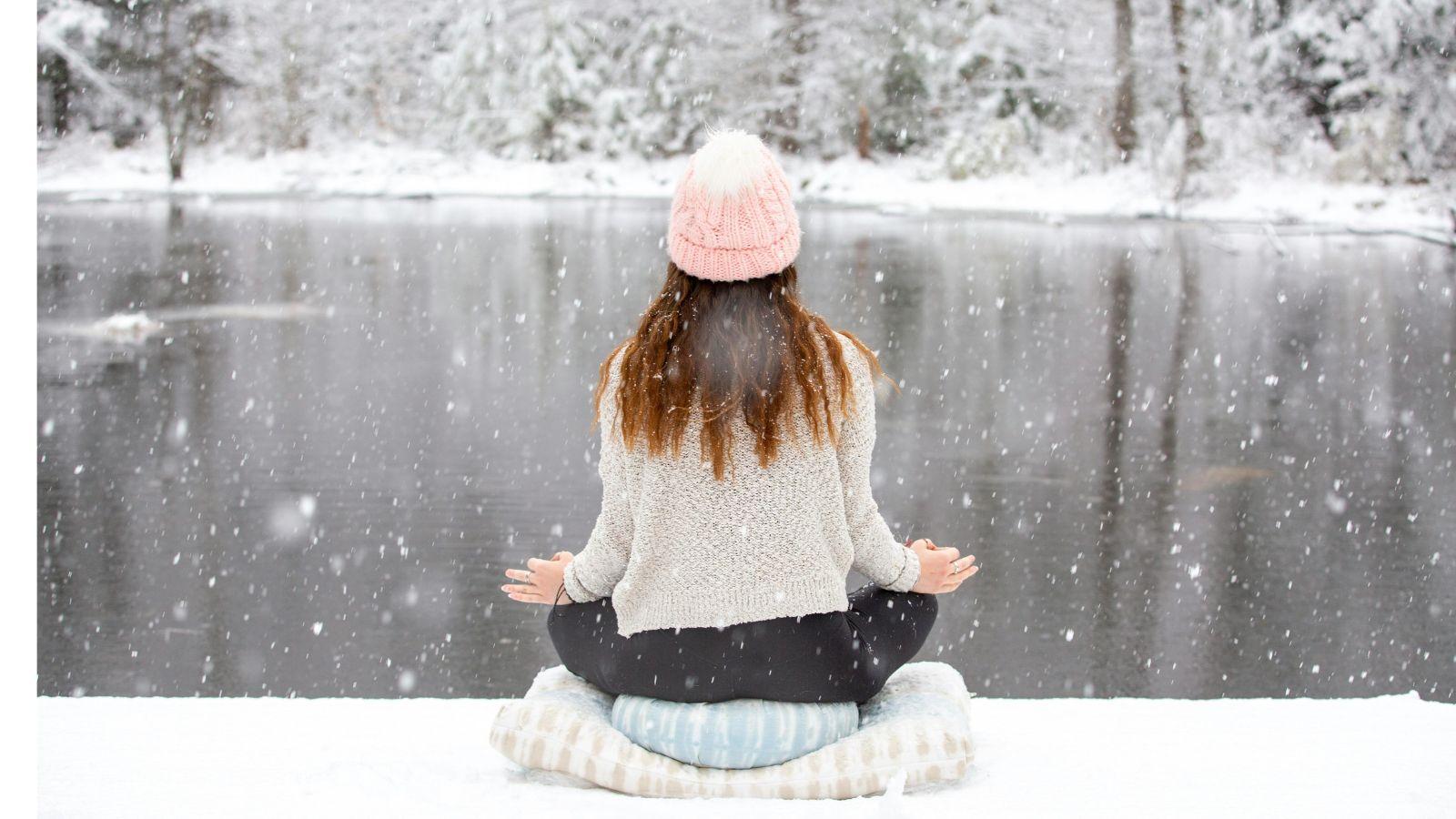 image of a lady next to a snowy lake, doing a yoga pose to illustrate winter wellness