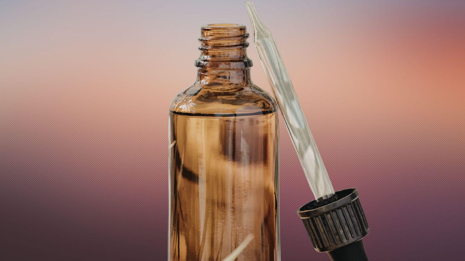 Vetiver image of vetiver essential oil in a bottle on a sunset background with the essential oil dropper propped up on the bottle