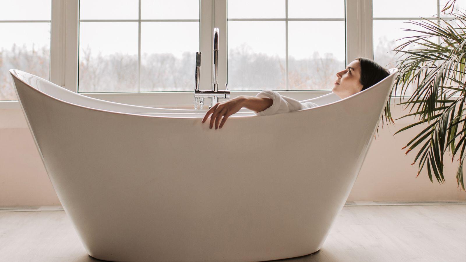 vetiver essential oil can be used in the bath image of a woman soaking in a big free standing bath by a window